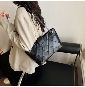 Detail of black quilted leather shoulder bag with silver chain strap and metal lock