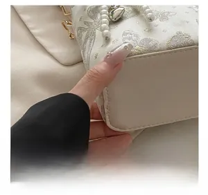 Dettaglio del ricamo a farfalla e ciondolo a perla su borsa in jacquard color crema