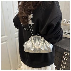 Close-up of shiny silver pleated clutch bag with pearl handle and metal chain strap