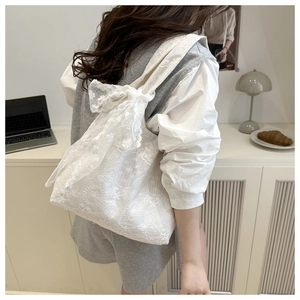 Detail of white lace floral tote bag with a large bow showing elegant embroidery texture