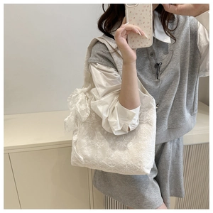 Close-up of white lace tote bag featuring 3D floral embroidery and a large side bow