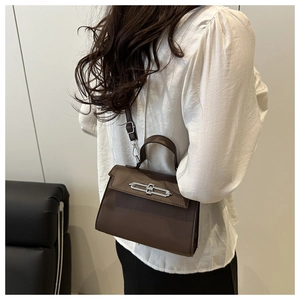 Detail view of a dark brown leather Kelly bag with silver lock worn by a model
