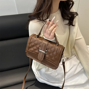 Brown quilted crossbody bag with silver buckle and top handle shown on a white dress