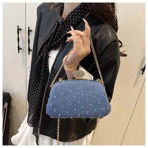 Detail of blue denim handbag featuring frayed tassels, crystal buckle and gold chain strap