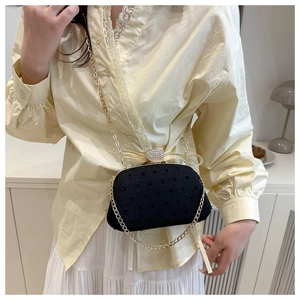Detail of elegant black textured crossbody bag with rhinestone buckle and gold chain strap