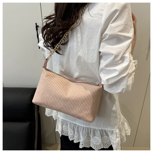 Detail of a light pink woven shoulder bag with golden chain strap on white lace shirt