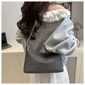 Détail du sac bandoulière tissé noir et blanc avec chaîne dorée porté par un mannequin