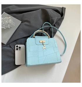 Detail of light blue crossbody bag with crocodile texture, metal handle and deer charm