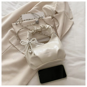 Λεπτομέρεια κρεμ τσάντας με σούρες, πέρλα φιόγκο και λουράκι με αλυσίδα