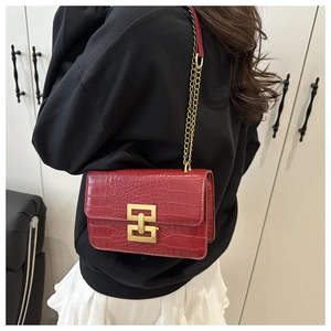 Detail of red crocodile pattern crossbody bag with golden geometric clasp and chain strap