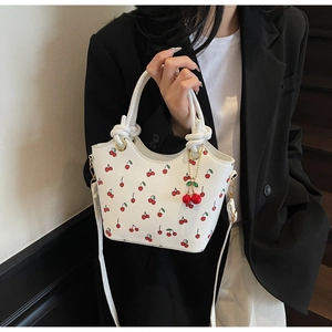 Détail du sac seau blanc avec imprimé cerise, poignée tressée et breloque cerise 3D