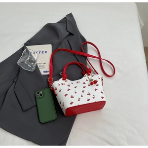 Détail du sac à main blanc à motif cerises avec base en cuir rouge et breloque cerise