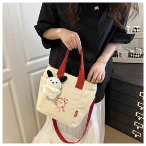 Detail of canvas tote bag with red handles, cartoon bear print and plush puppy charm