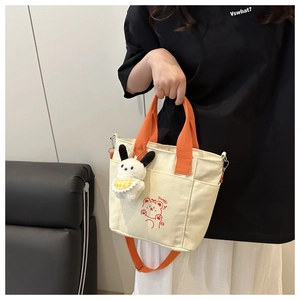 Detail of canvas tote bag featuring orange handles, cartoon bear print, and rabbit charm