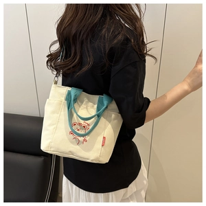 Detail of canvas tote bag with blue handles and red bear print worn by a model