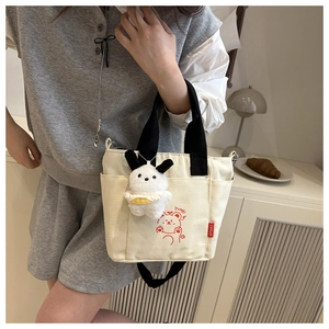 Lifestyle view of white canvas crossbody bag with red cartoon bear and plush dog charm