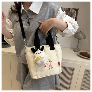 Detail of canvas tote bag with red bear print and plush charm on shoulder strap