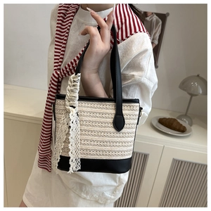 Chic beige straw bucket bag with black leather trim and lace ribbon on a model