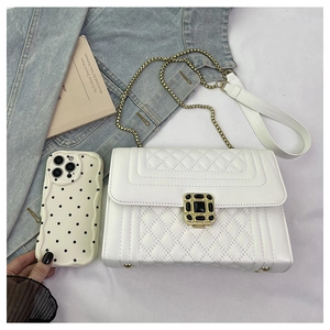 Detail of white quilted crossbody bag with gold chain strap and ornate gemstone clasp