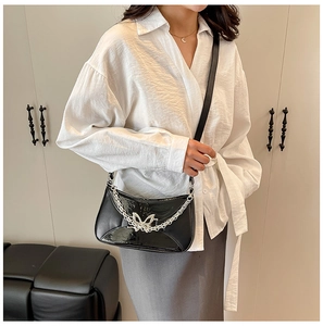 Detail of a black chic shoulder bag featuring a silver butterfly buckle and chain