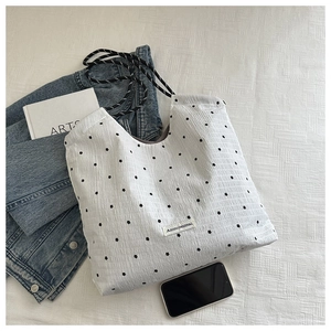 Detail of white polka dot tote bag featuring floral patterns and a woven drawstring strap