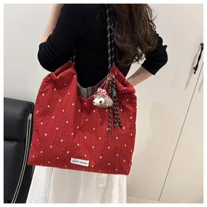 Detail of red floral tote bag with rope handle and plush bear charm on model shoulder