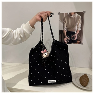 Detailed texture of black floral corduroy tote bag with rope handles and plush charm