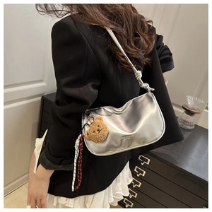 Detail of silver crescent shoulder bag featuring a cute bear charm and fashion text