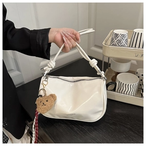 Detail of cream pillow bag with knot handle and plush bear charm in a lifestyle setting
