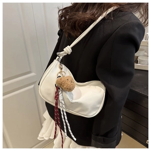 Detail of white hobo bag with knotted strap and cute plush bear charm on model shoulder