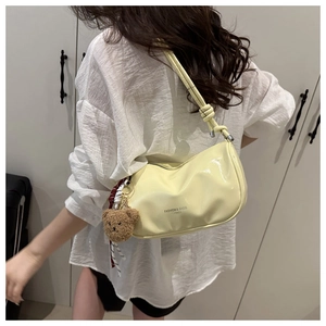 Detail of pale yellow patent leather pillow bag with cute brown teddy bear charm