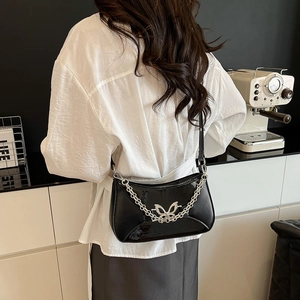 Chic black glossy shoulder bag with silver butterfly buckle and chain on a female model