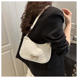 Detail of white woven crescent shoulder bag with golden bow hardware and leather trim