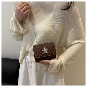Close-up of brown quilted crossbody bag with star ornament and silver chain on model