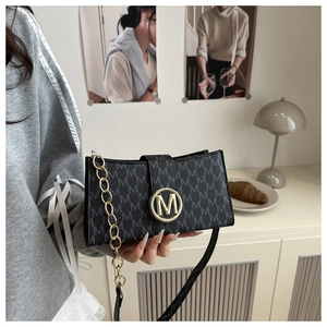 Close-up of golden M-letter magnetic buckle and chain on black leather shoulder bag