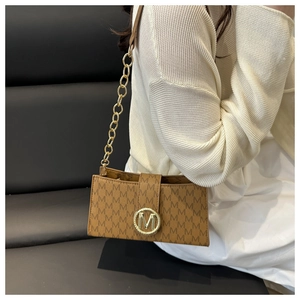 Detail of a brown shoulder bag with gold M-logo, chain strap, and elegant monogram print