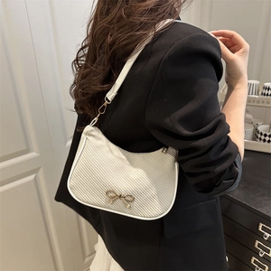 Chic beige woven shoulder bag with gold bow accessory shown on model's shoulder