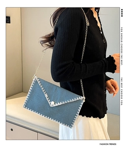 Sac enveloppe en denim bleu avec coutures en zigzag blanches, perle et chaîne dorée