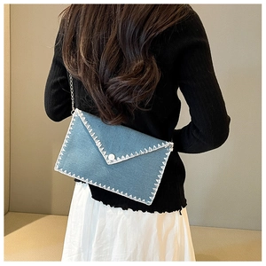 Détail du sac enveloppe en denim bleu avec surpiqûres zigzag blanches et chaîne argentée