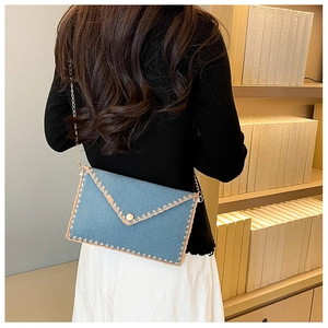Détail du sac enveloppe en jean bleu clair avec dentelle crochetée et chaîne dorée