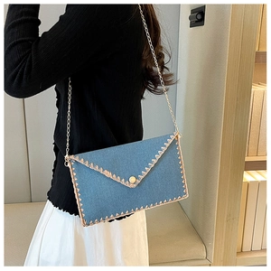 Détail du sac enveloppe en denim bleu avec surpiqûres beiges et bandoulière chaîne
