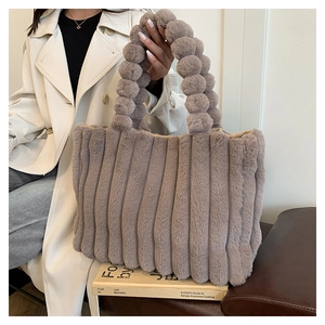 Detail of taupe plush tote bag featuring vertical stripe texture and pom-pom handle