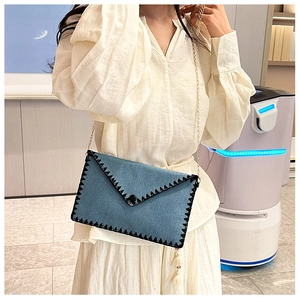 Détail du sac enveloppe en denim bleu avec bandoulière chaîne et coutures zigzag