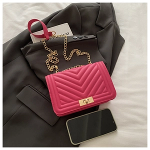 Détail du sac bandoulière rose matelassé en V avec chaîne dorée sur fond de blazer