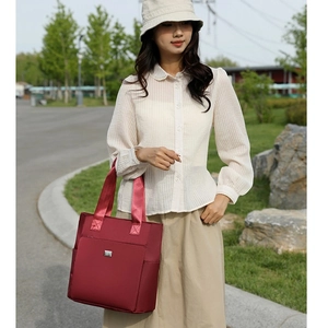Red stylish nylon tote bag with reinforced handles shown in a park setting