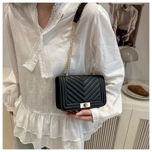 Détail d'un sac bandoulière matelassé noir avec chaîne dorée et fermoir porté par un mannequin