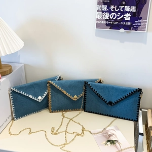 Sac enveloppe en denim bleu avec coutures contrastées et bandoulière en chaîne