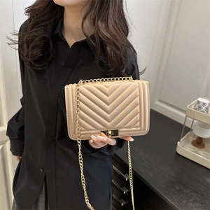 Sac bandoulière beige matelassé en V avec chaîne dorée porté par un mannequin