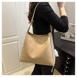 Detail of a beige large capacity tote bag worn as a shoulder bag on a model