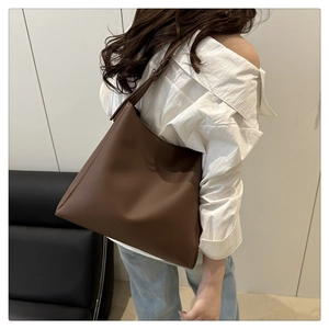 Detail of a large dark brown tote bag with adjustable strap worn by a model in a city setting